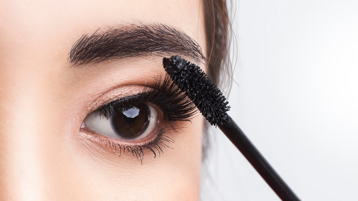 Close-up of a mascara brush coating long upper lashes
