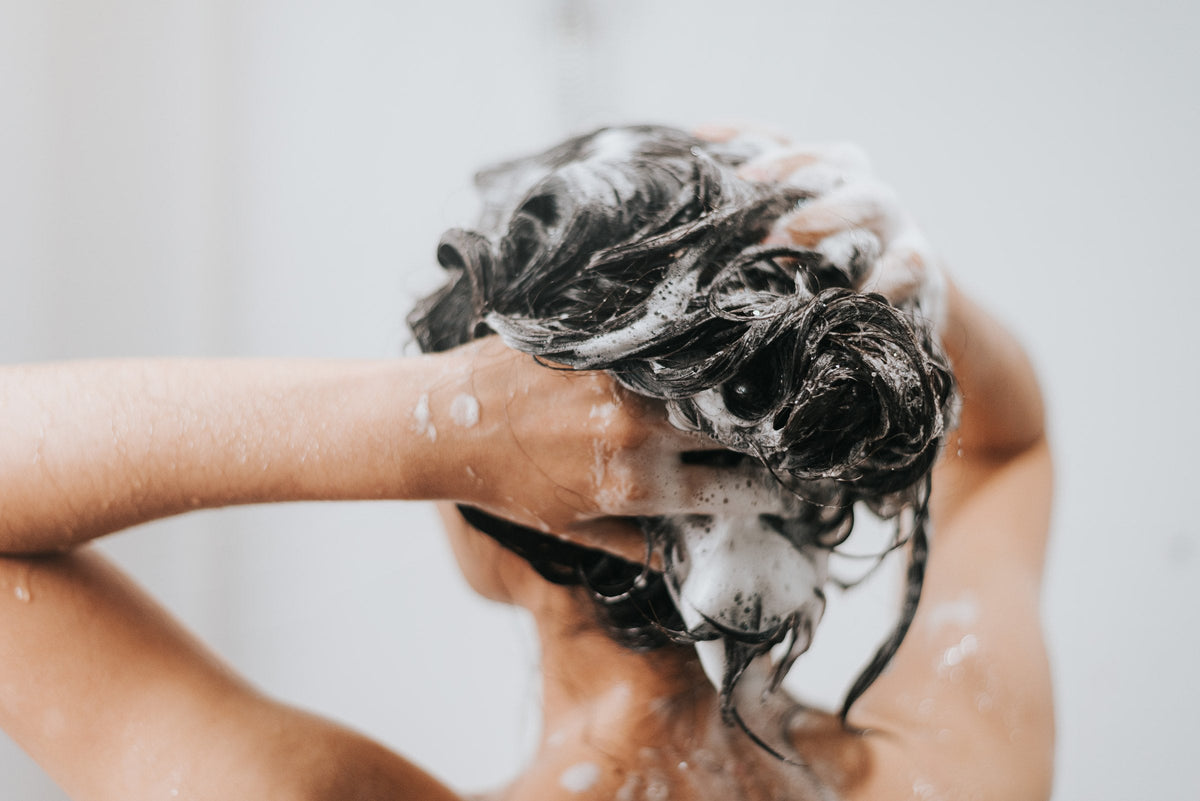 A woman lathering shampoo into her scalp in the shower