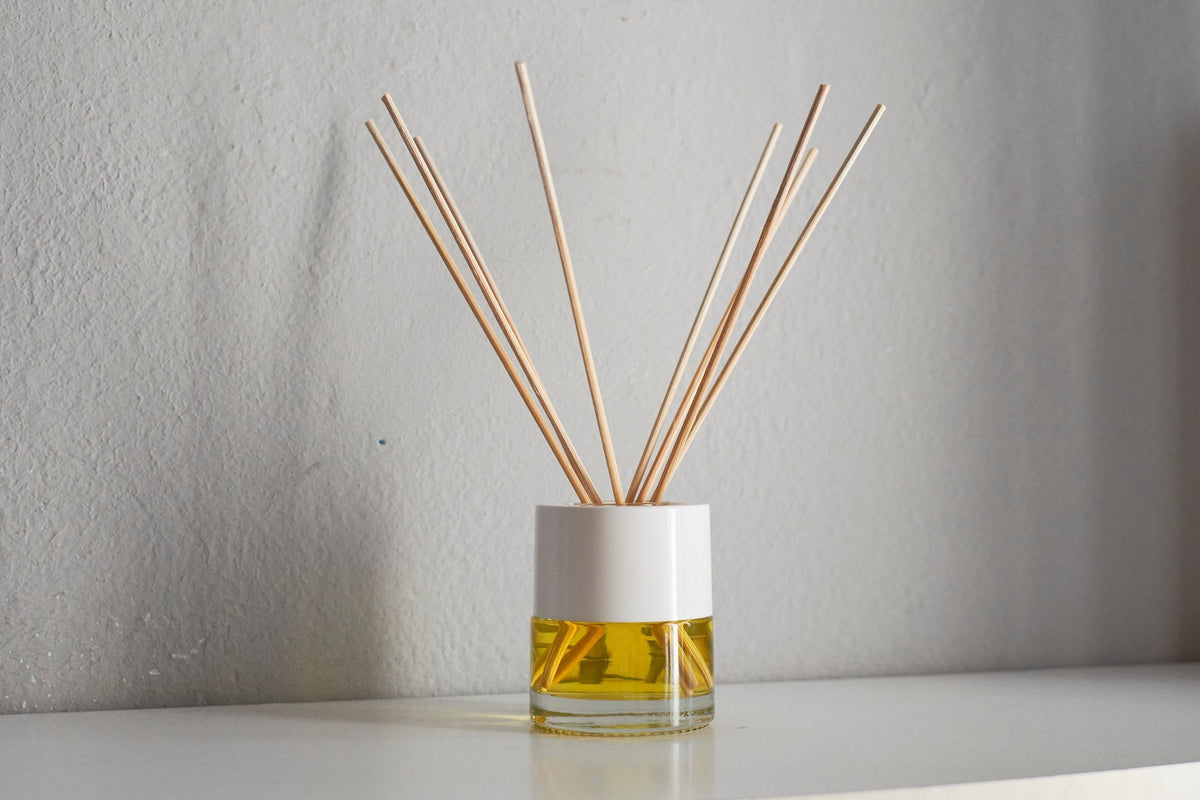 A reed diffuser with natural rattan sticks in a white and glass bottle of golden oil on a white table