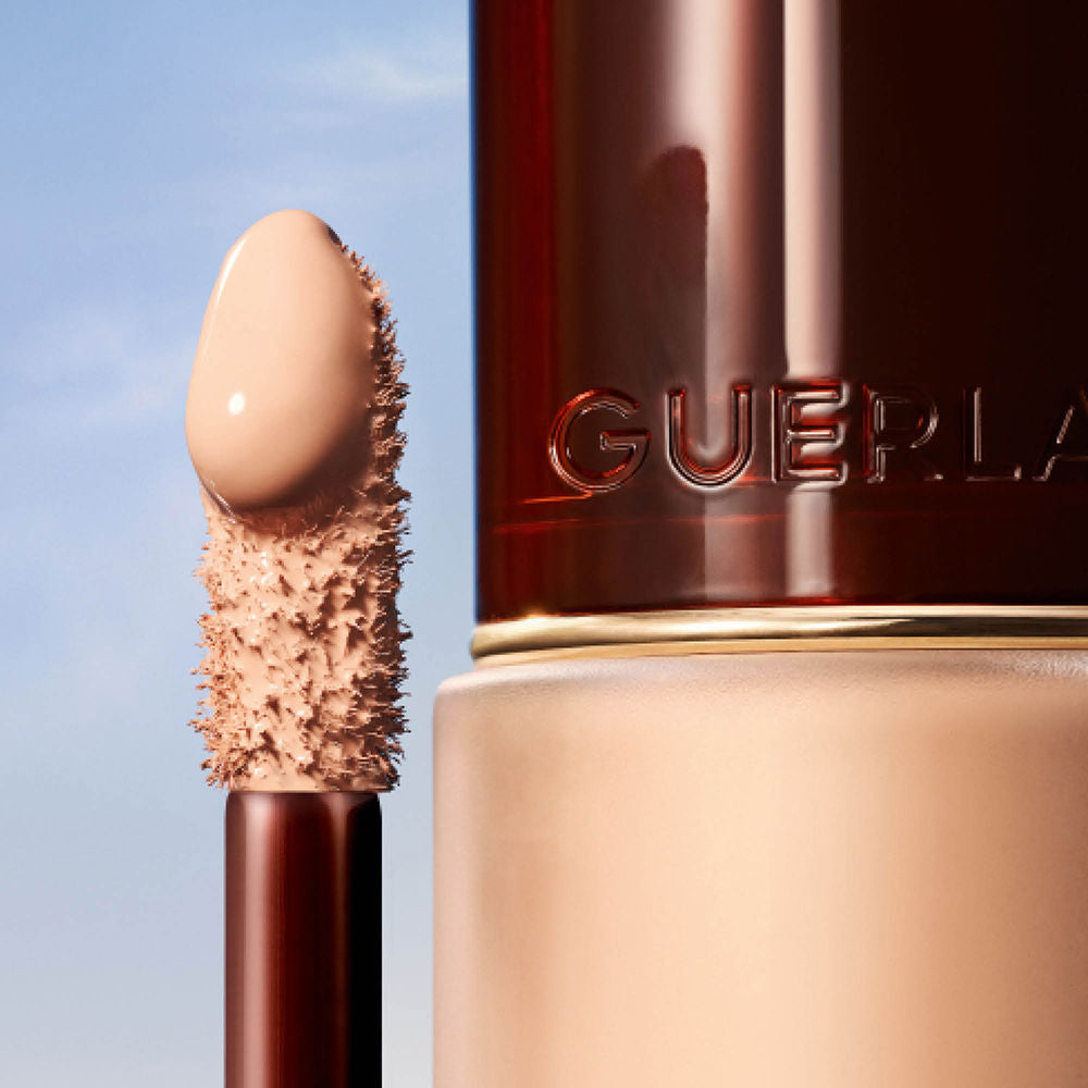 Guerlain Beige and dark brown liquid concealer in transparent cylindrical bottle with metallic cap and wand.